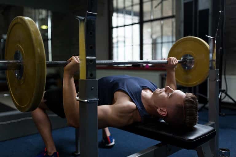 young man flexing muscles with barbell in gym