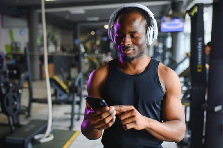 Athletic man standing in a gym listening to music using wireless headphones