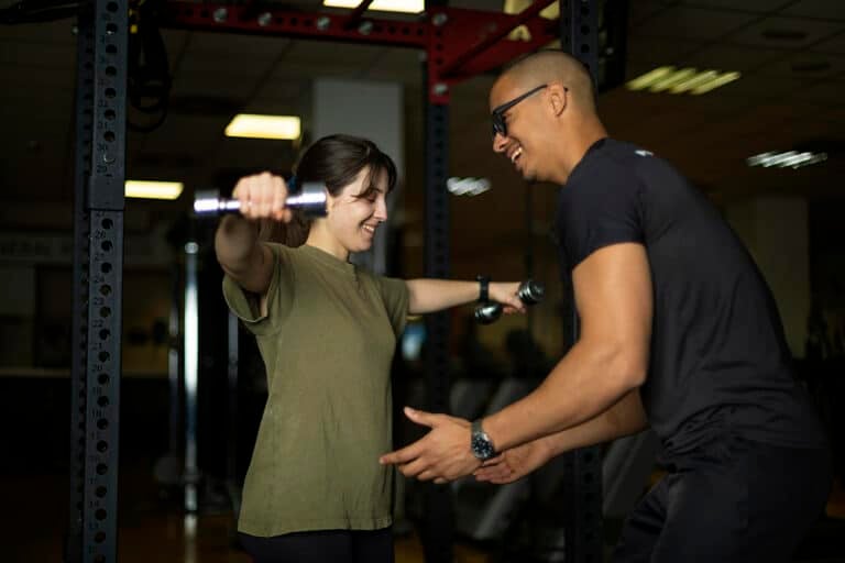 Smiling woman lifts dumbbells with coach's assistance at the gym