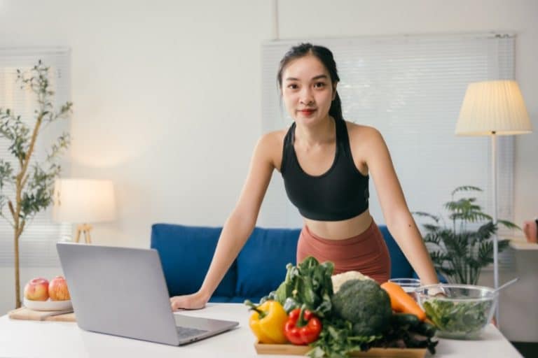 Young asian nutritionist woman working with laptop and fresh vegetables recommending a healthy diet in a modern and bright living room