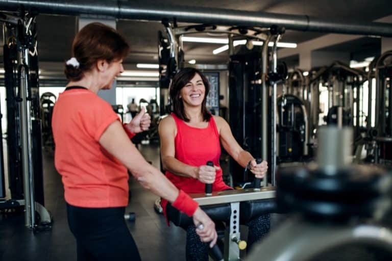 Two cheerful senior women in gym doing strength workout exercise