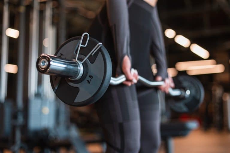 Healthy strong fitness trainer woman in black sportswear working out and trains with a bar and exercising in the gym