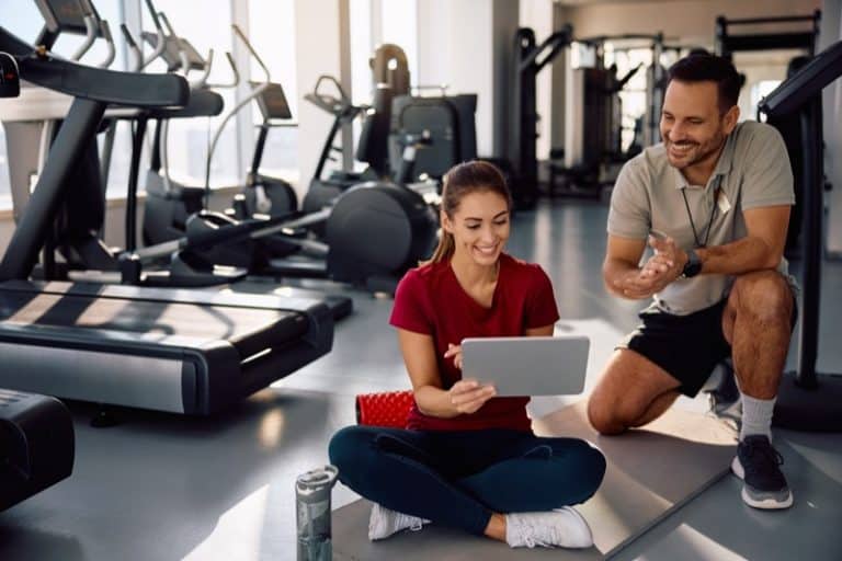 Happy athletic woman and her fitness instructor using digital tablet at the gym